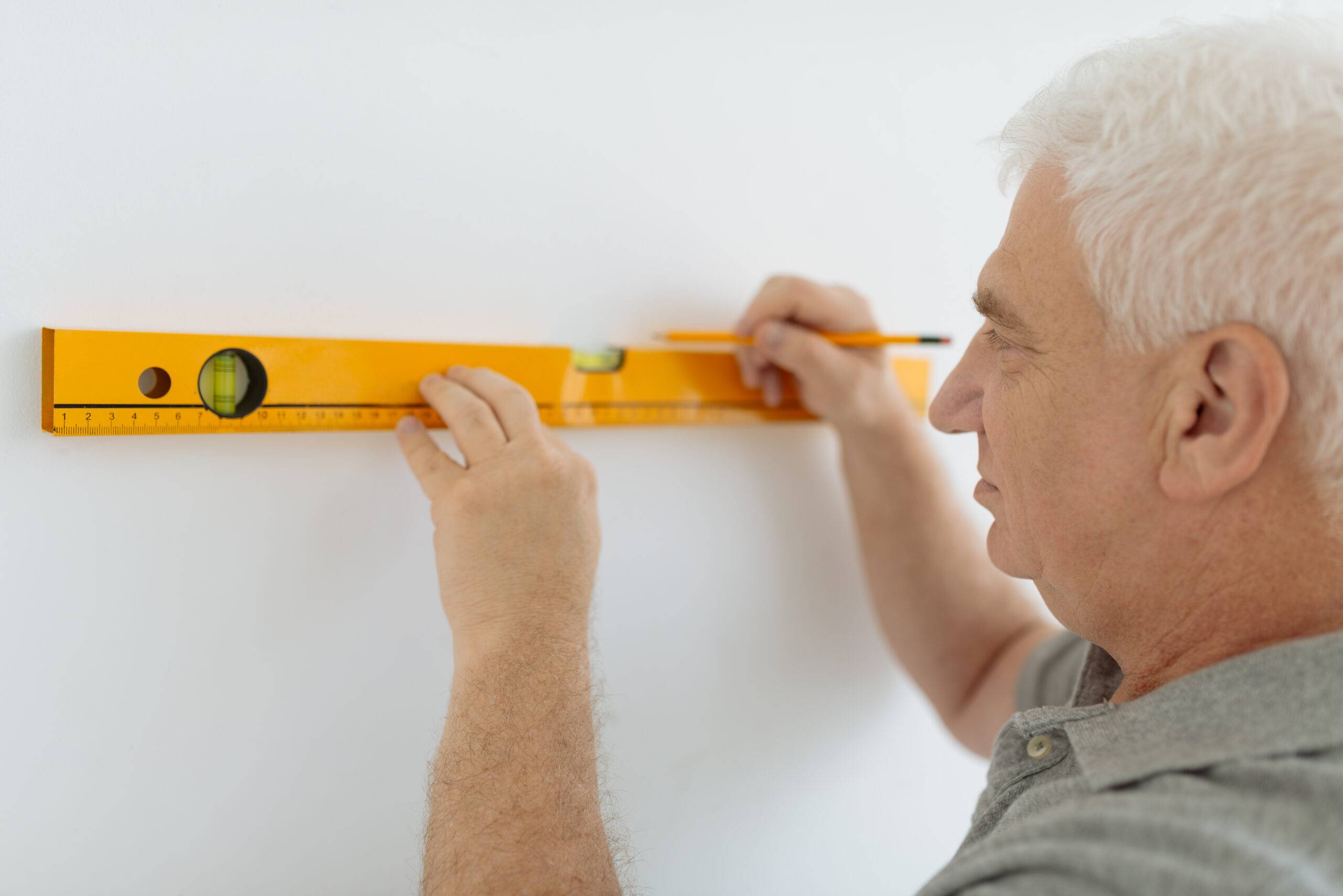Senior man measuring wall with construction level