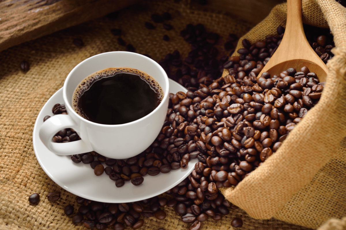 white cup of coffee on white saucer with bag of beans spilling over