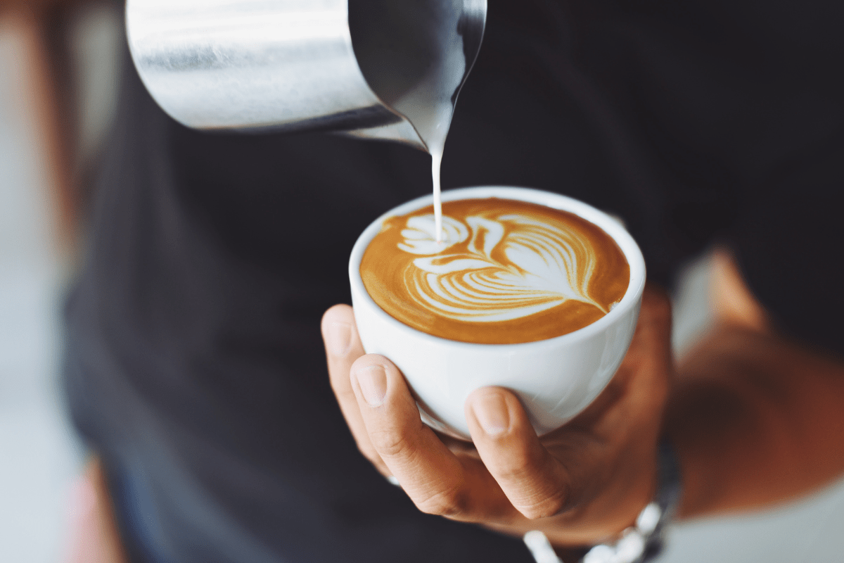 barista holding latte cup pouring milk to make design on top