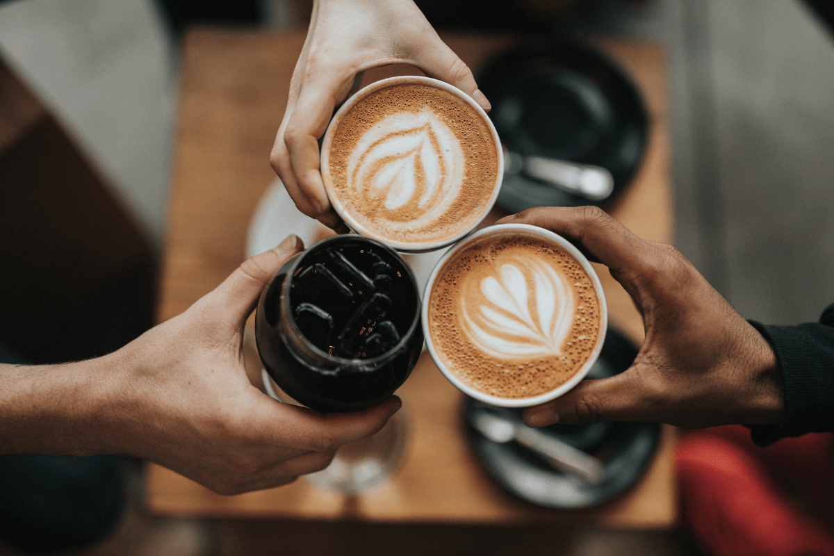 hands holding trio of cold and warm coffee drinks with latte art