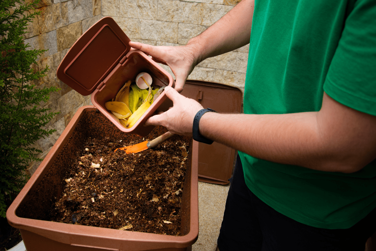 man in green shirt depositing food scraps into backyard compost bin