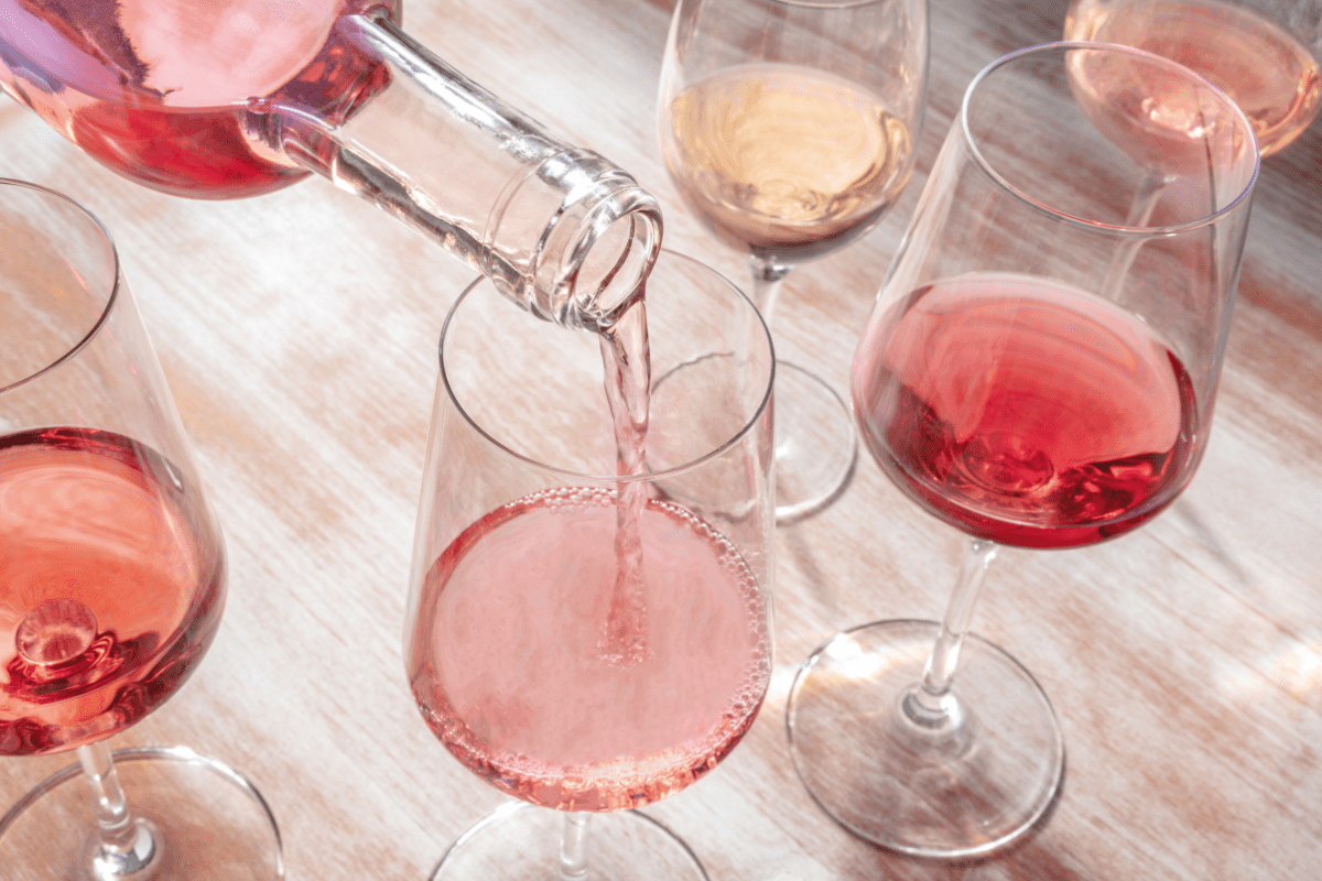 multiple wine glasses filled with rose on wooden table, with bottle filling one glass