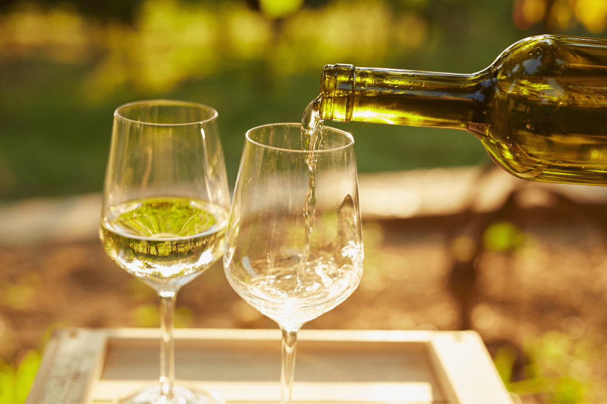 two wine glasses on outdoor table, bottle pouring white wine into glasses