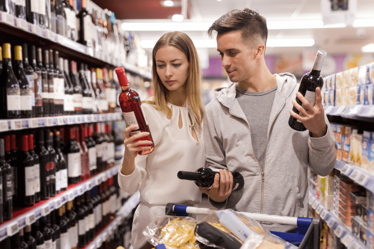 couple at grocery store choosing between multiple bottles of wine