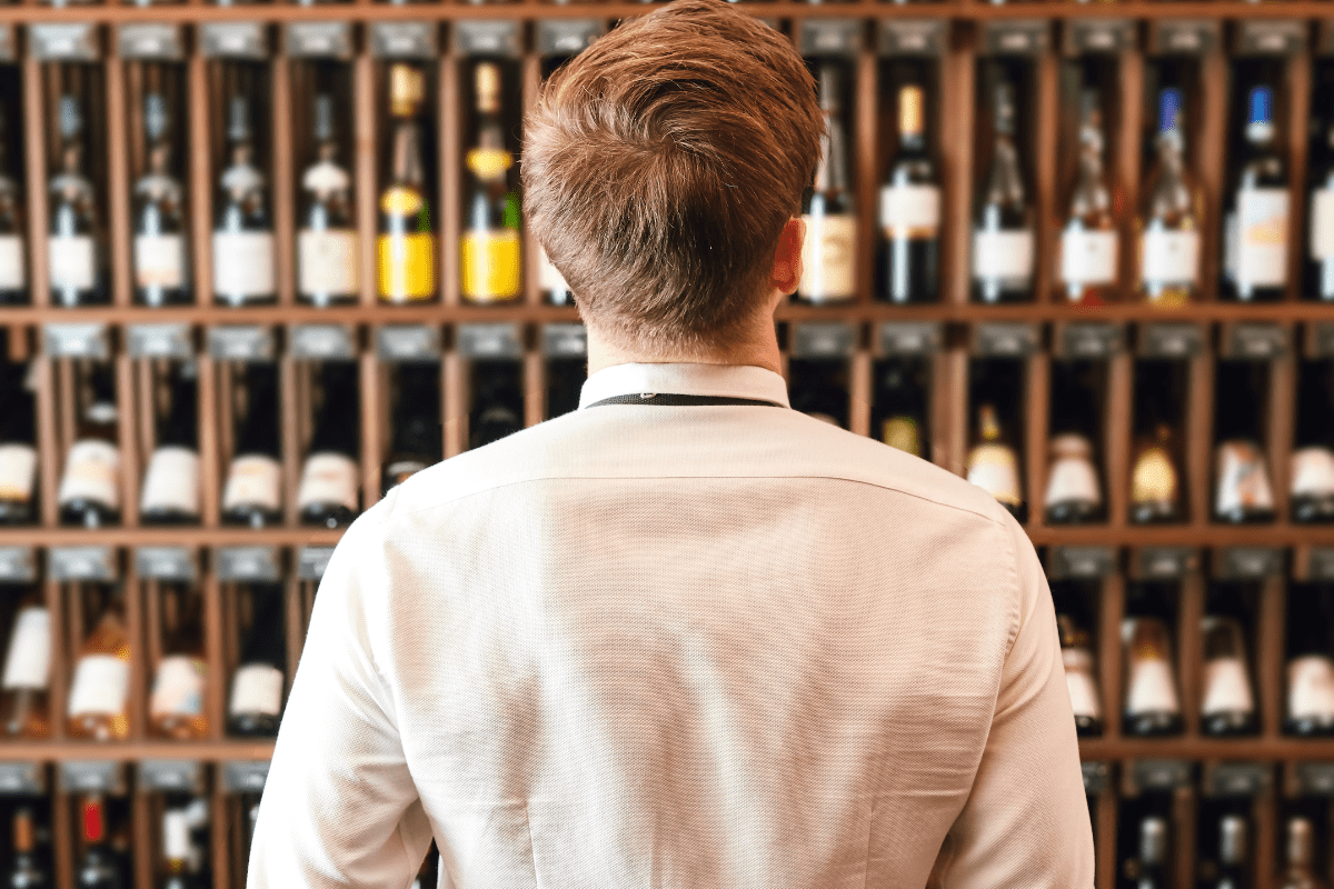 back of man in white shirt facing display of wine bottles