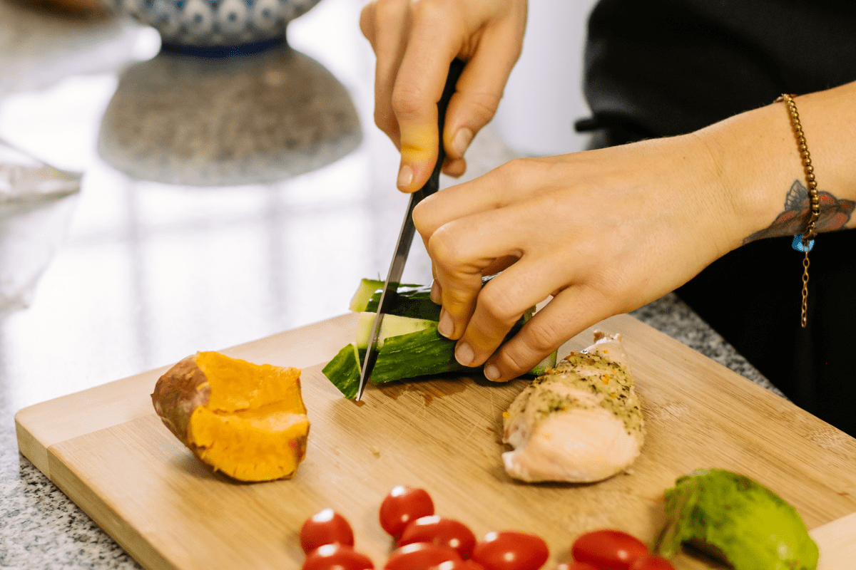 close up of woman chopping cucumber on wooden cutting board