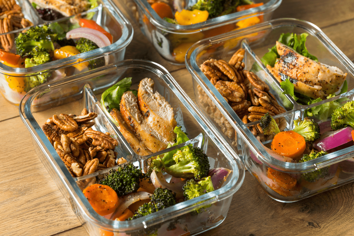 4 rectangular glass tupperware containers full of prepped food including chicken and roast vegetables