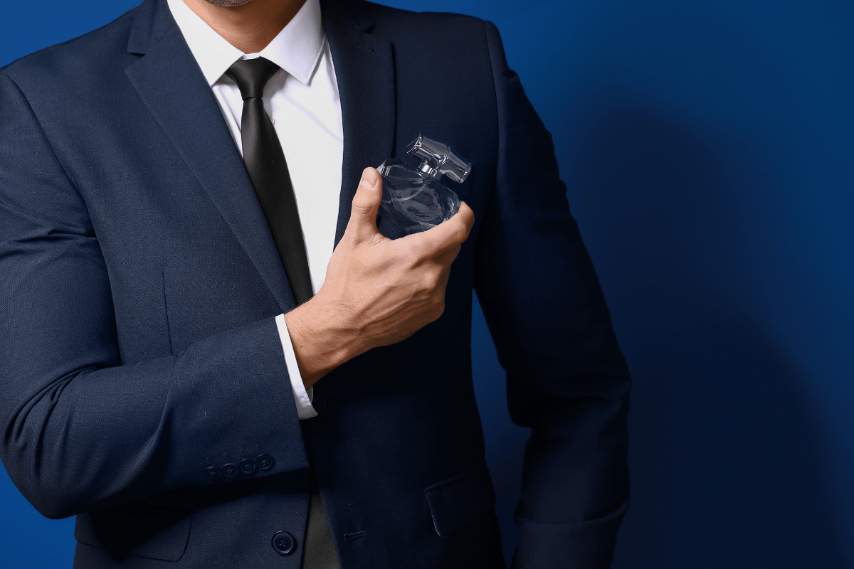 man in blue suit holding bottle of cologne