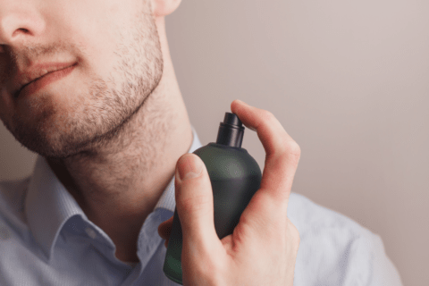 close up of man with beard spraying cologne on neck
