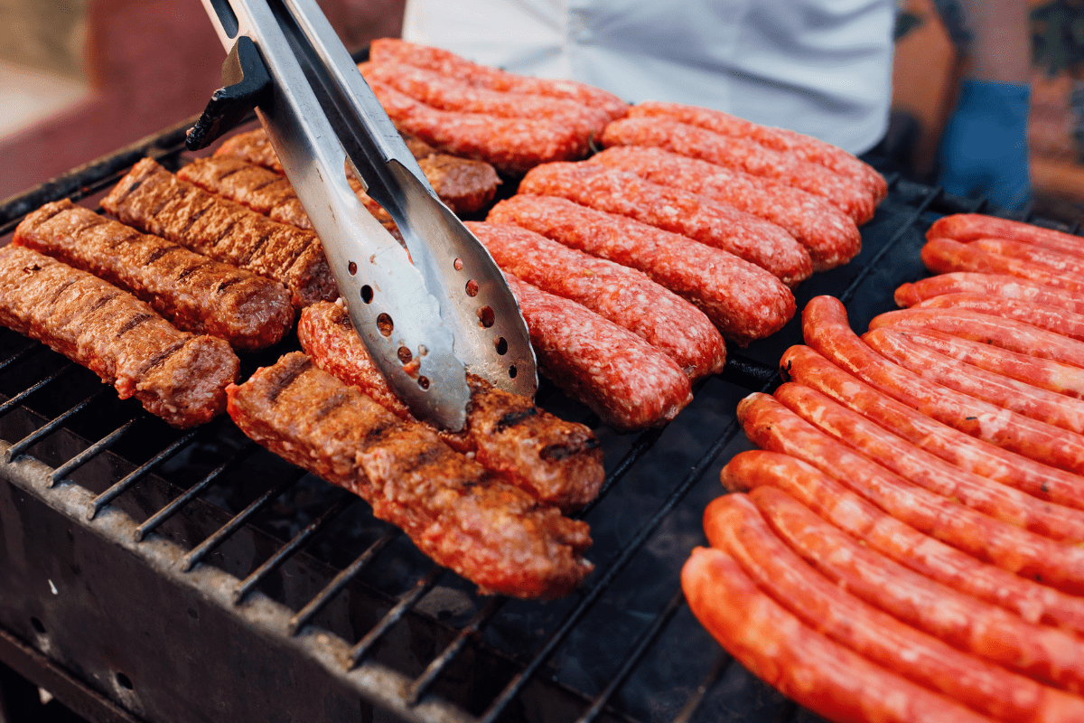 close up of meat cooking on grill sausages metal tongs