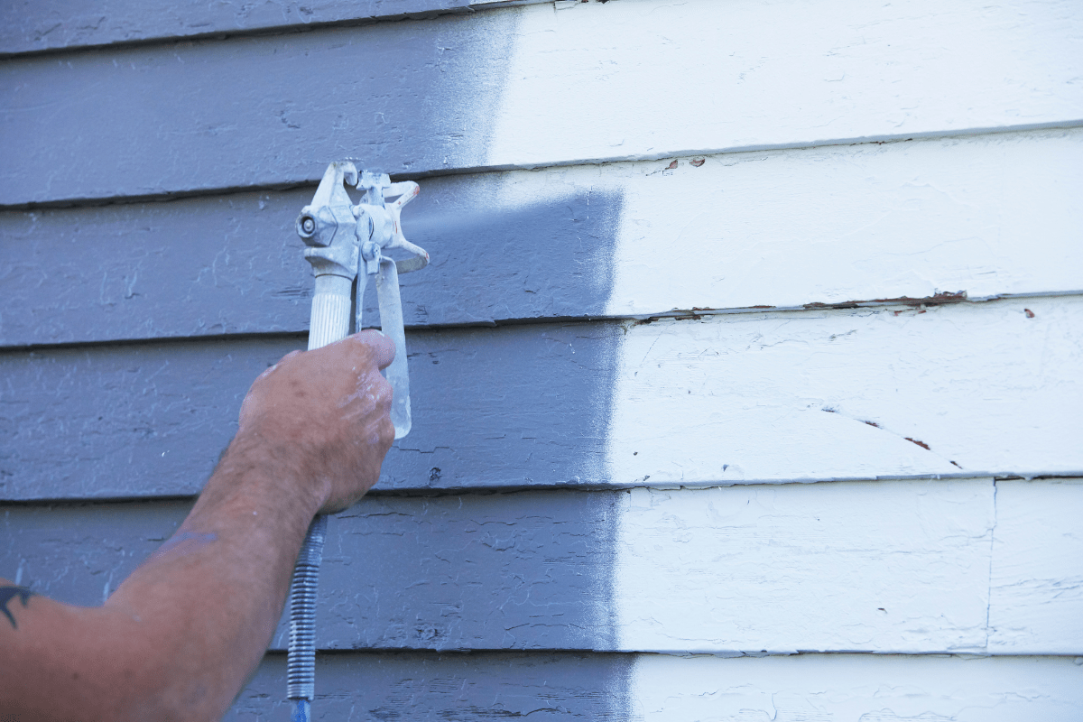 close up of hand spraypainting outside of house exterior siding