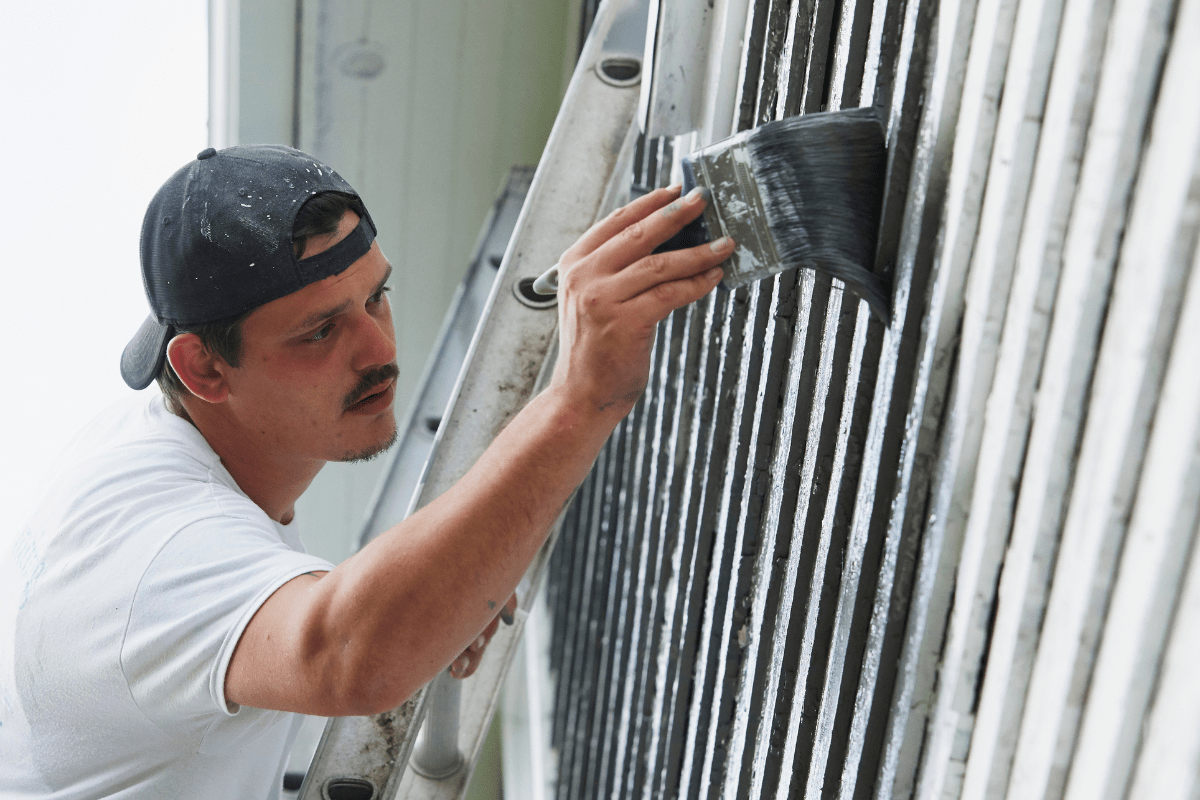 close up of a man painting the exterior siding of a house