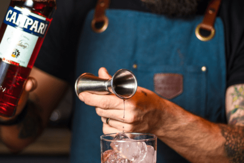 close up of a man making a cocktail with a stainless steel jigger