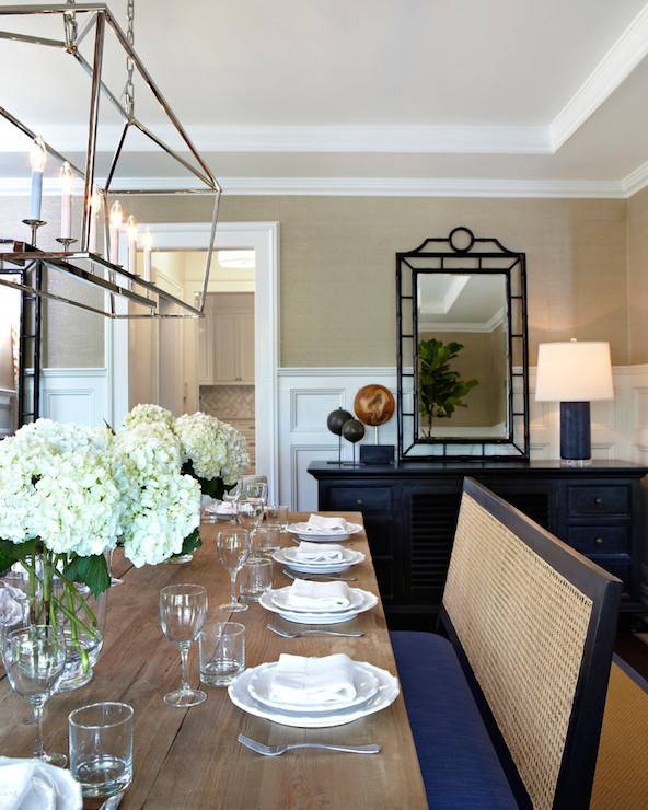 Brilliant dining room features Darlana Linear Pendant illuminating Restoration Hardware Salvaged Wood Trestle Rectangular Extension Dining Table lined with cane back bench. Formal dining room boasts gold grasscloth on upper walls and stacked wainscoting on lower walls framing Bungalow 5 Chloe Mirror leaning against black buffet cabinet topped with navy blue lamp.