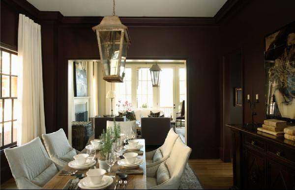 Brown & gray formal dining space design with chocolate brown walls, ivory drapes, rustic wood trestle dining table, white slipcovered chairs, lantern, art and buffet.