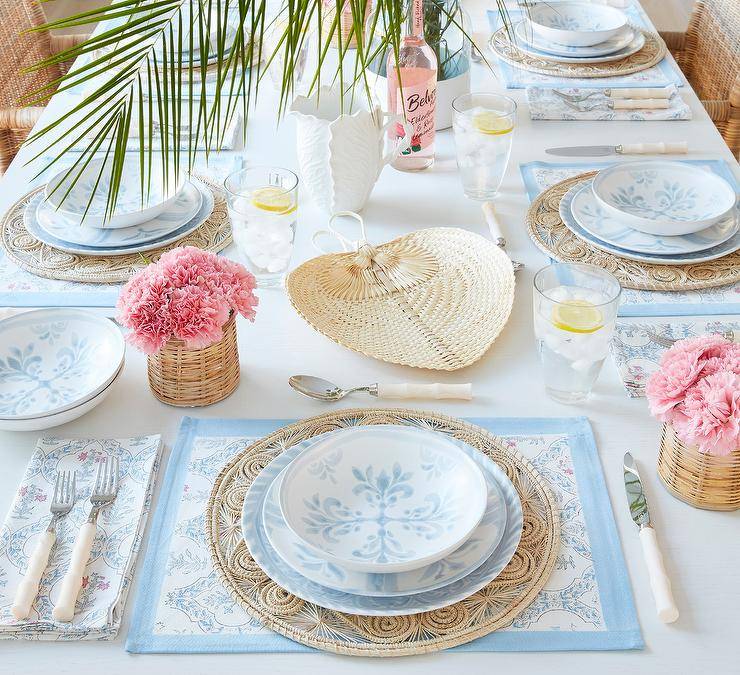 White and blue placemats sit beneath round rattan plate chargers placed under white and blue plates.