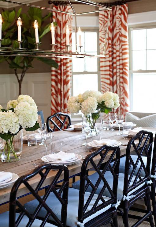 Fabulous dining room features Darlana Linear Pendant illuminating Restoration Hardware Salvaged Wood Trestle Rectangular Extension Dining Table lined with cane back bench and black bamboo chairs as well as upholstered captain chairs at each end of the table atop sisal rug. Formal dining room boasts gold grasscloth on upper walls and stacked wainscoting on lower walls framing bay window dressed in red zebra curtains flanked by fiddle leaf fig plants.