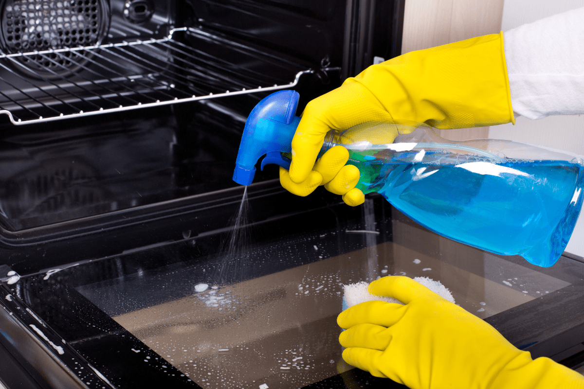 spraying glass cleaner on an oven door