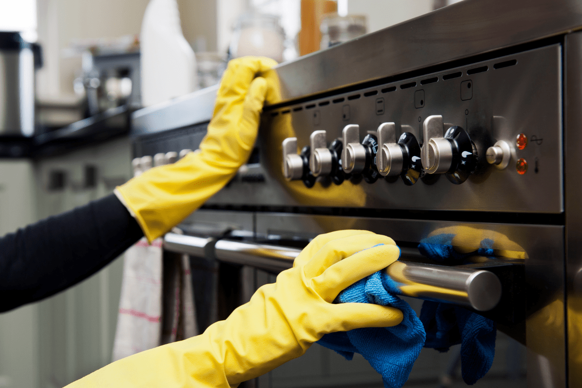 close up on exterior of gas oven with person wearing rubber gloves cleaning it