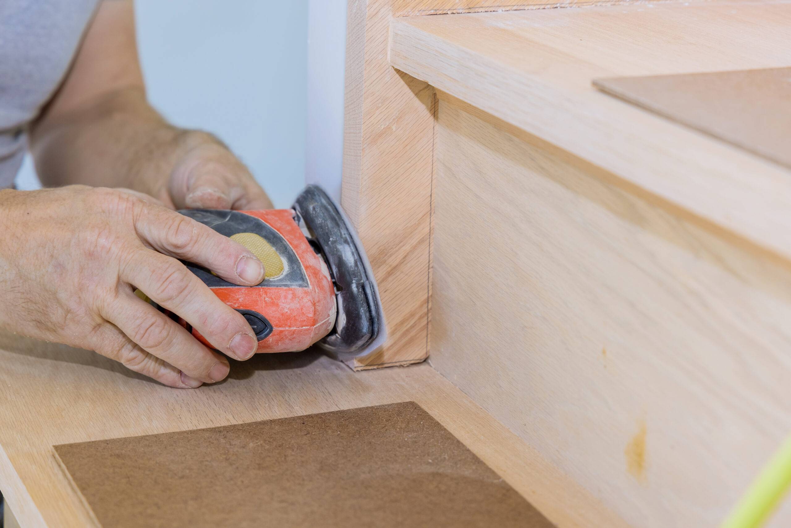 Grinding carpenter using polishing machine to refinish new home stairwell railings trims