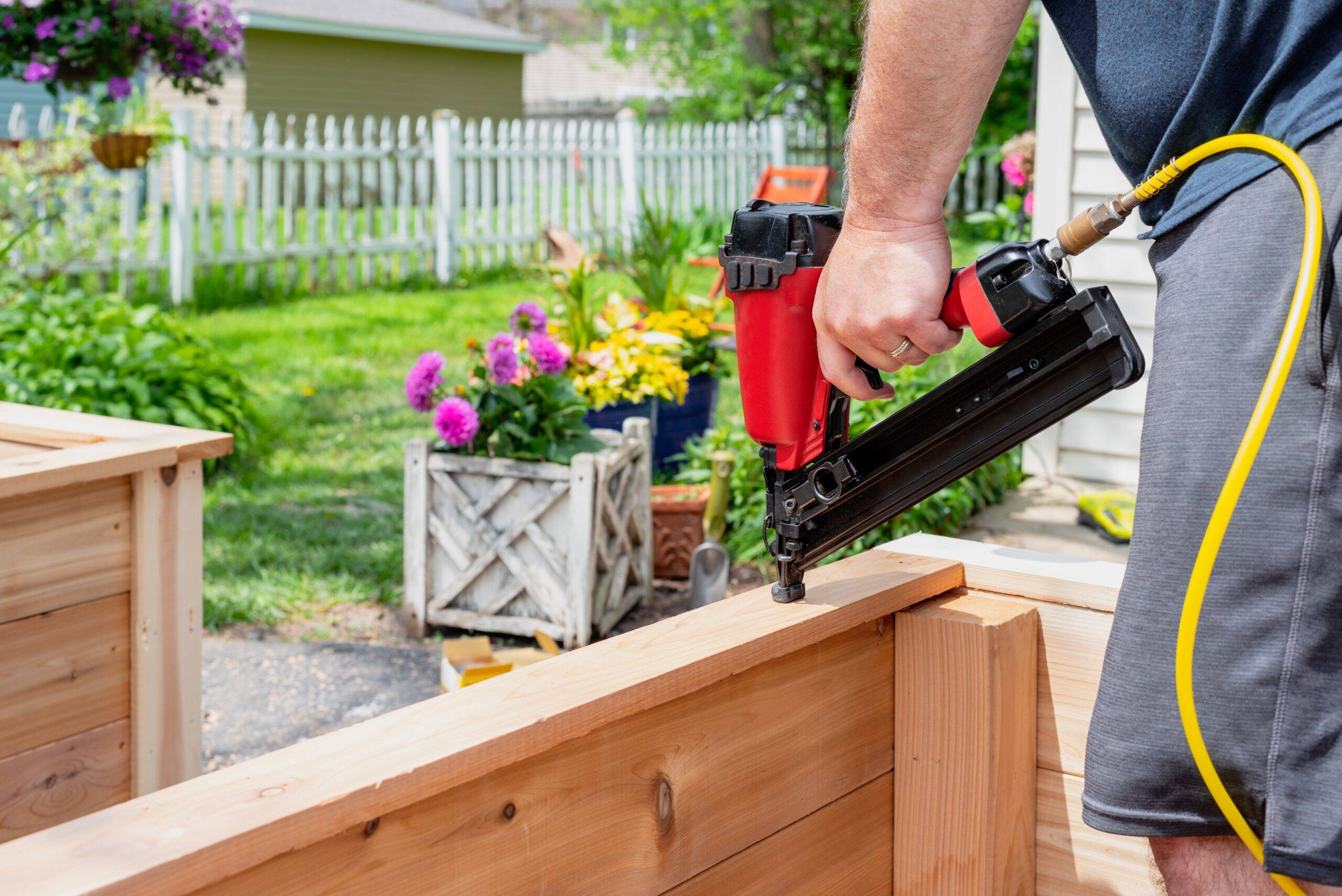 Closeup of a man using a pneumatic nail gun to finish the trim on cedar planters for the garden