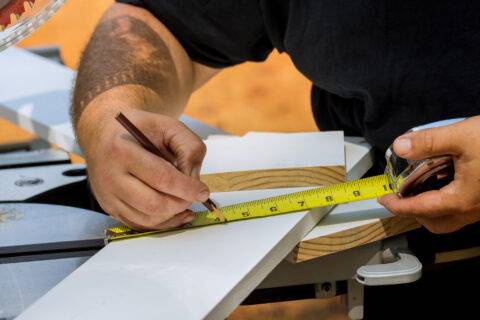 Woodworker preparation for sawing in man measures a piece of wood with tape measure