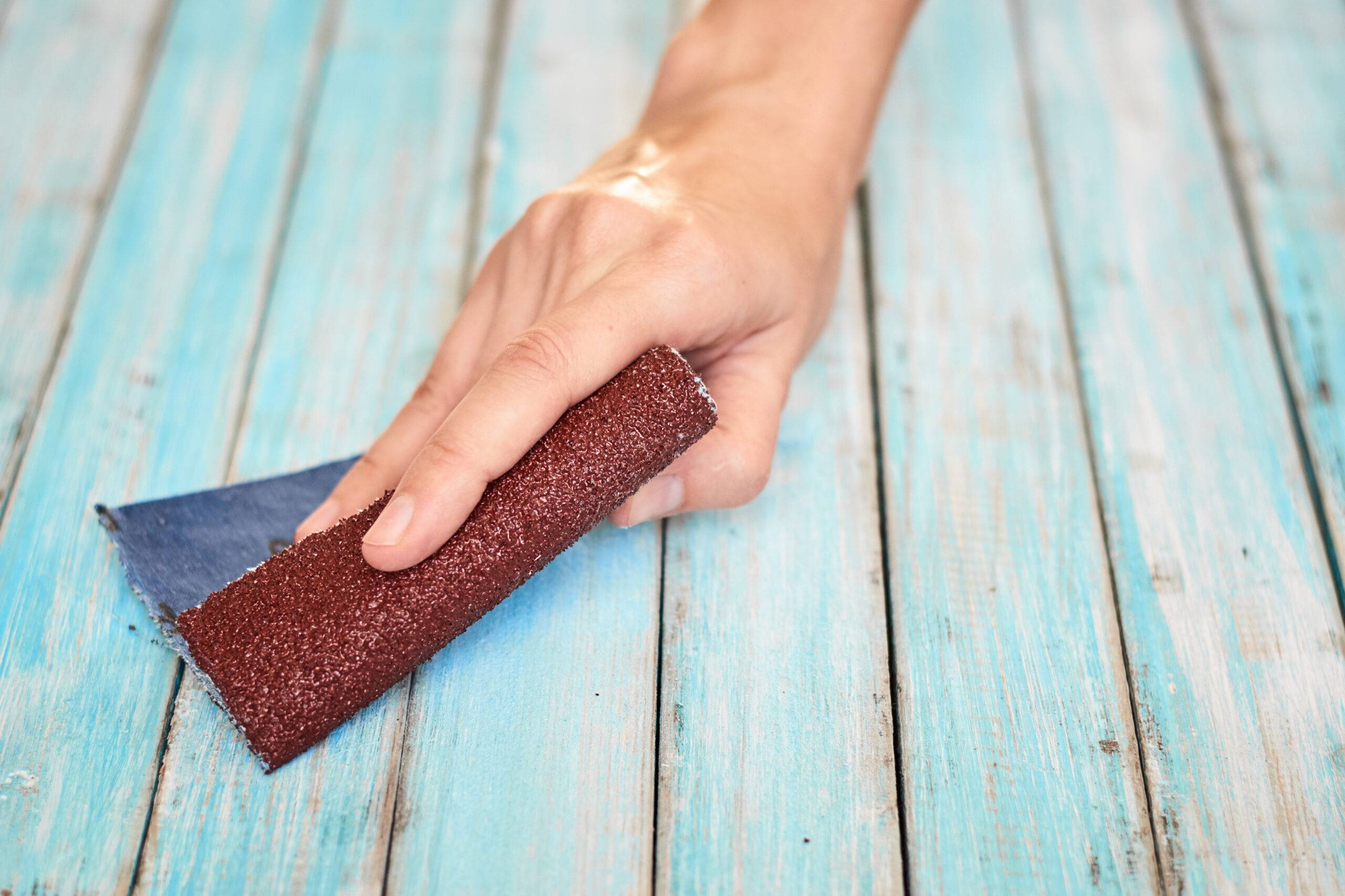 Hands sanding blue paint off wooden boards with sandpaper