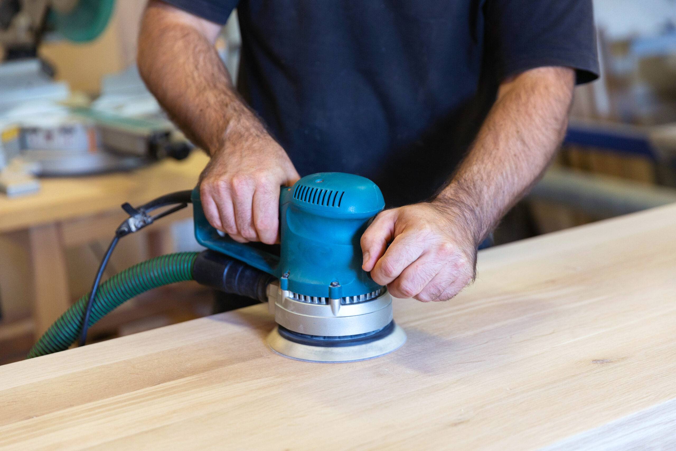 Sanding a wood surface with orbital sander in a workshop