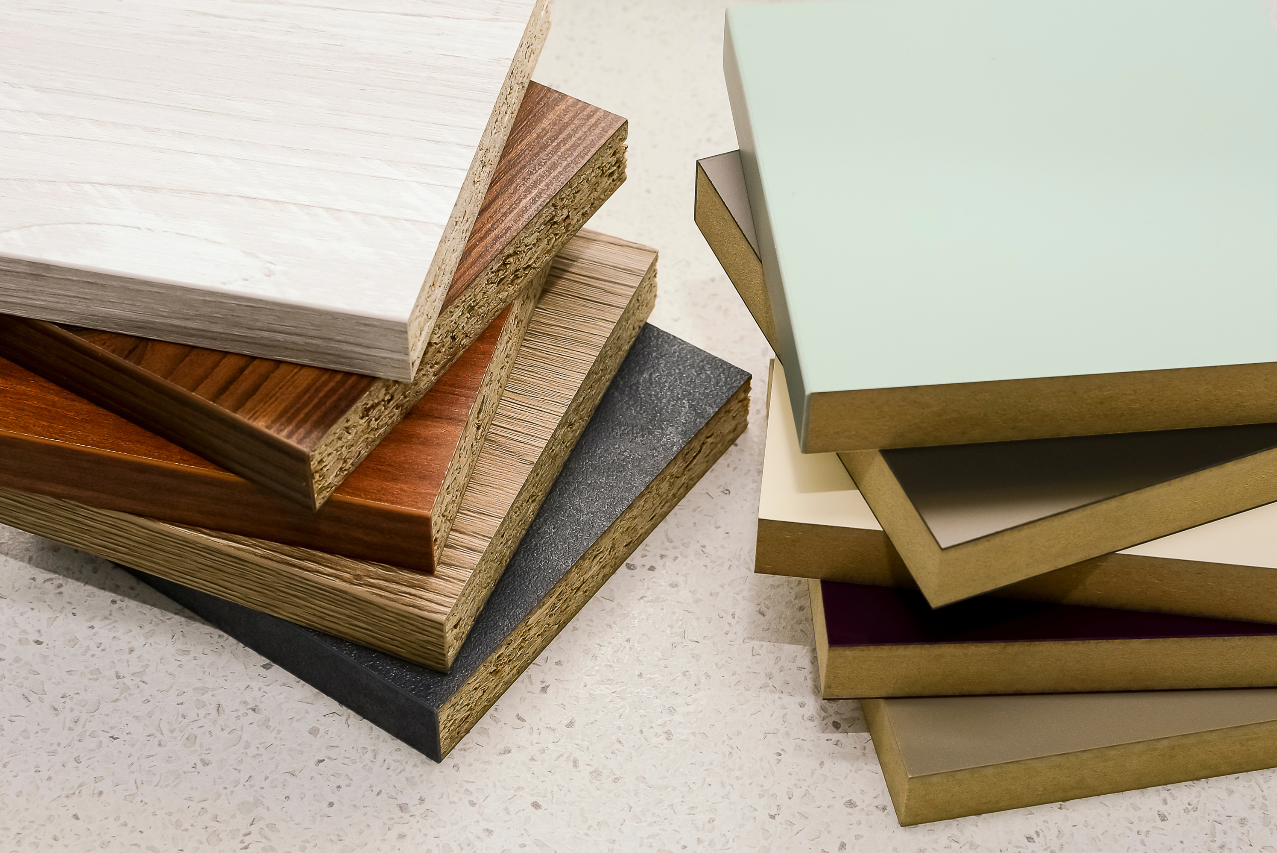 A stack of MDF samples in varying colors beside a stack of particle board samples