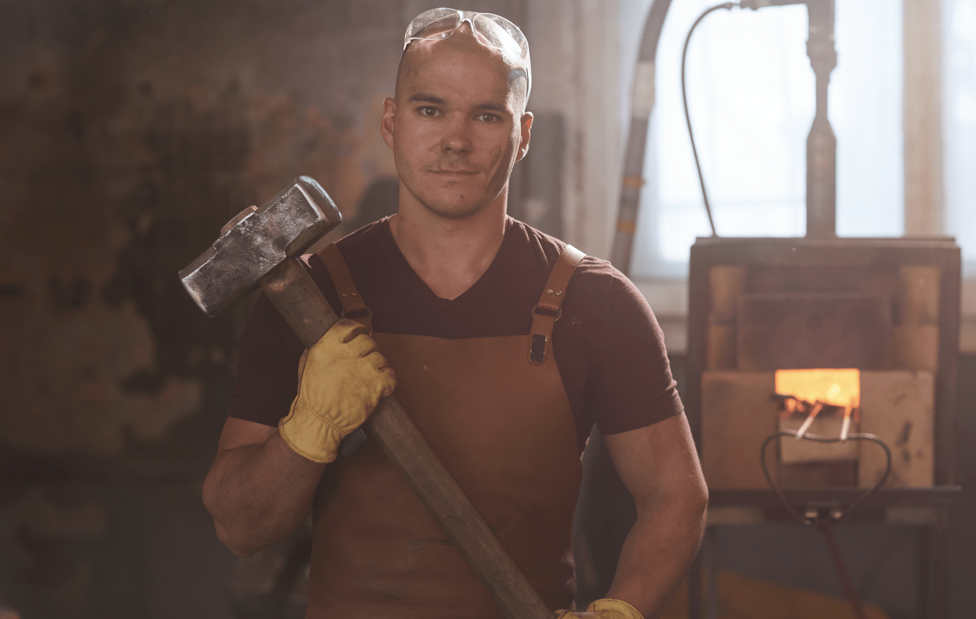 Man wearing safety glasses and work apron holding a sledgehammer.