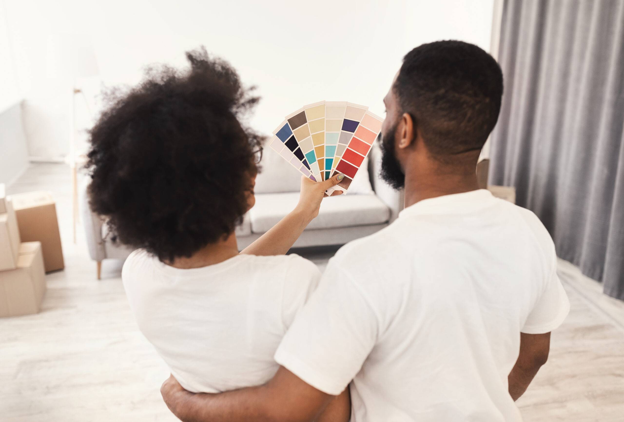 Couple choosing color for wall painting, holding color palette standing back to the camera at home.