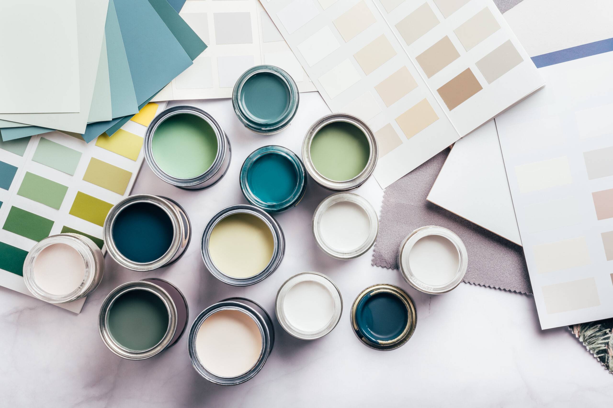 Tiny sample paint cans during house renovation, process of choosing paint for the walls, different green and beige colors, color charts on background.