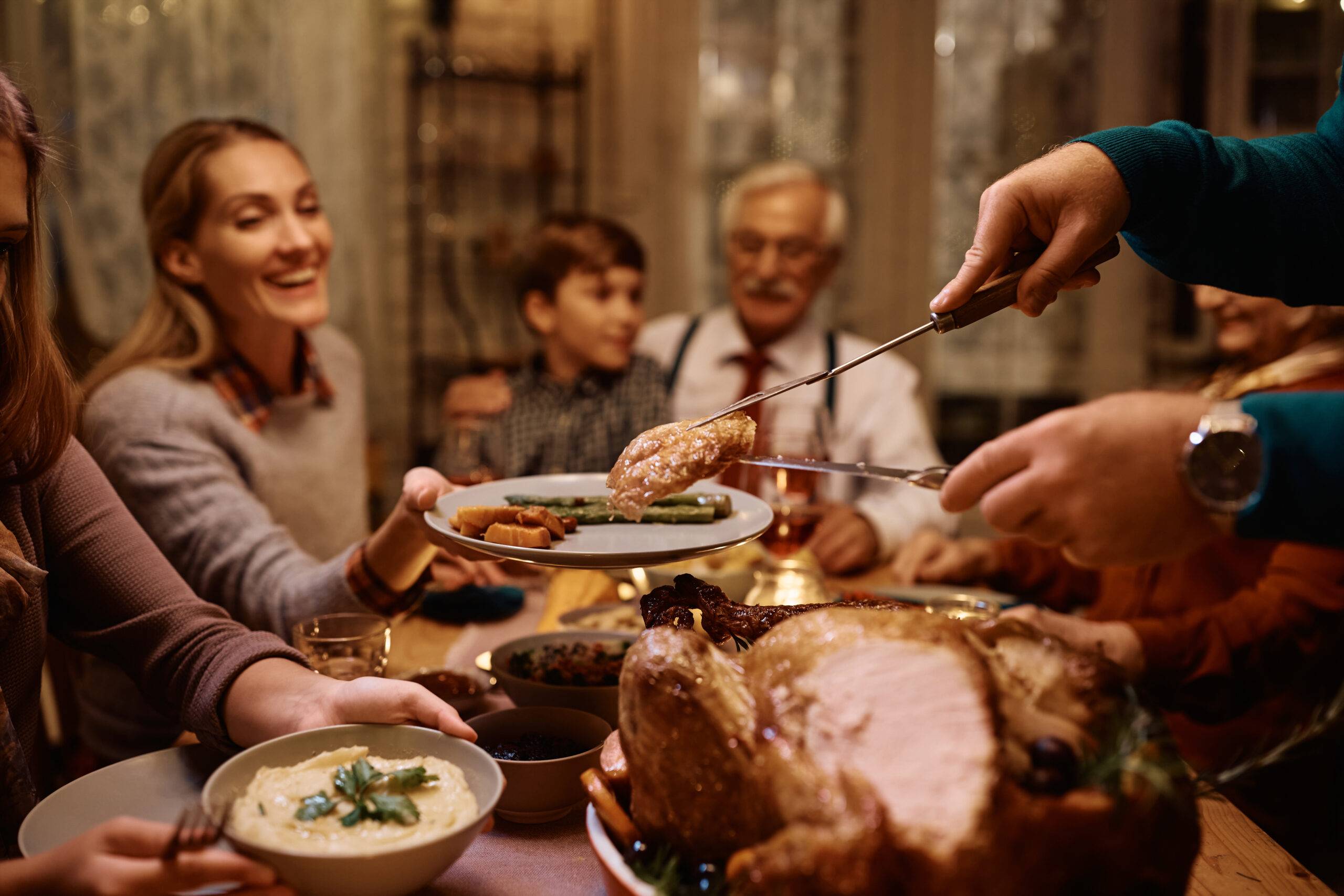 Close up of father serving Thanksgiving turkey to his extended family at dining table.