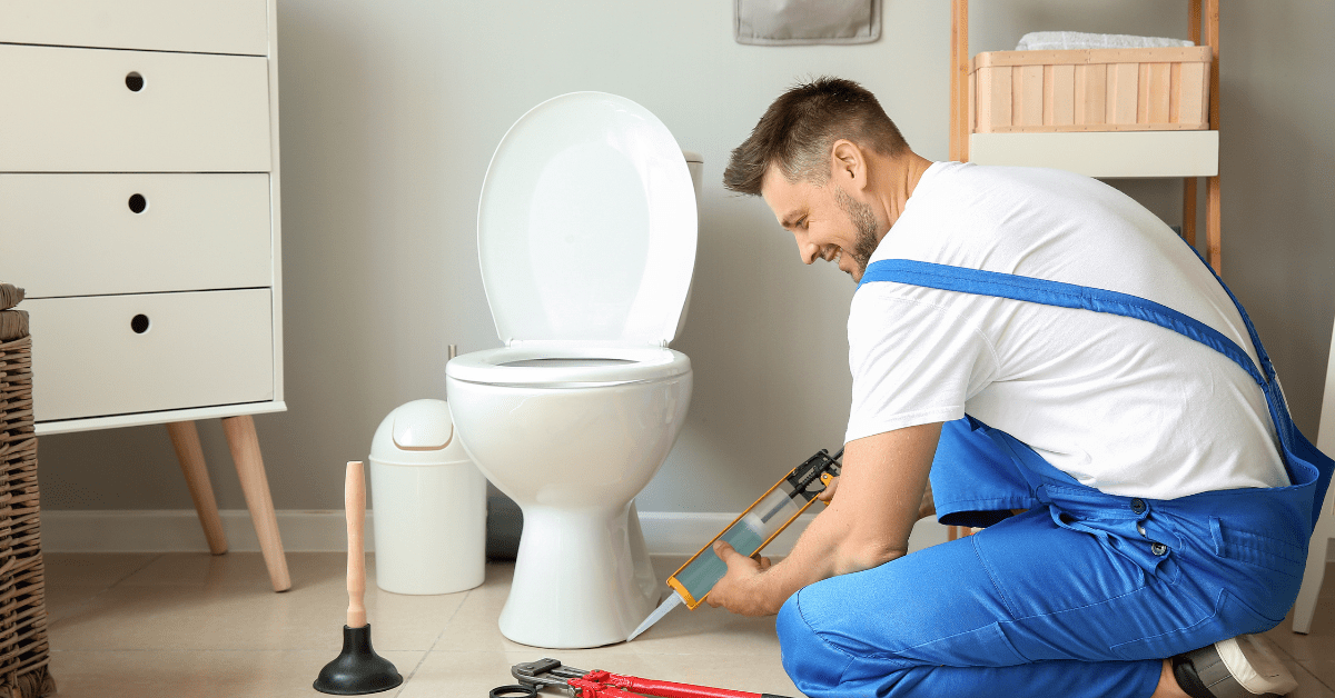 Worker sealing the toilet to the floor after installation.