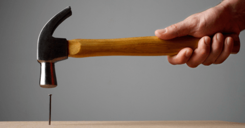 Hand holding a hammer above a nail in wood