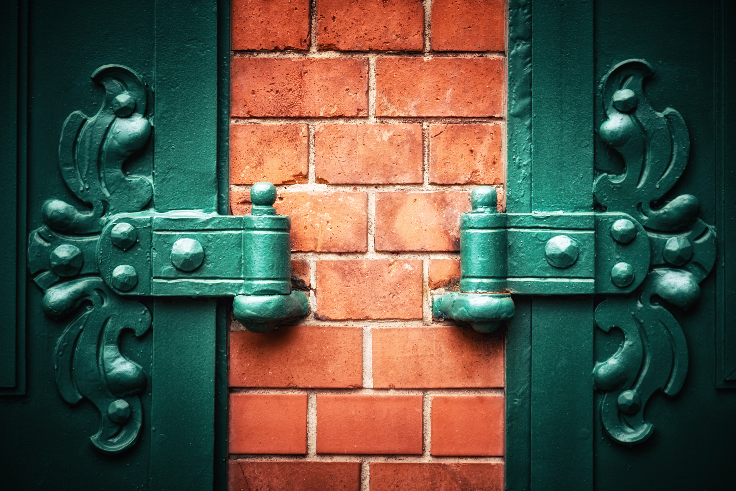 Closeup of a green specialty hinge on a brick wall.