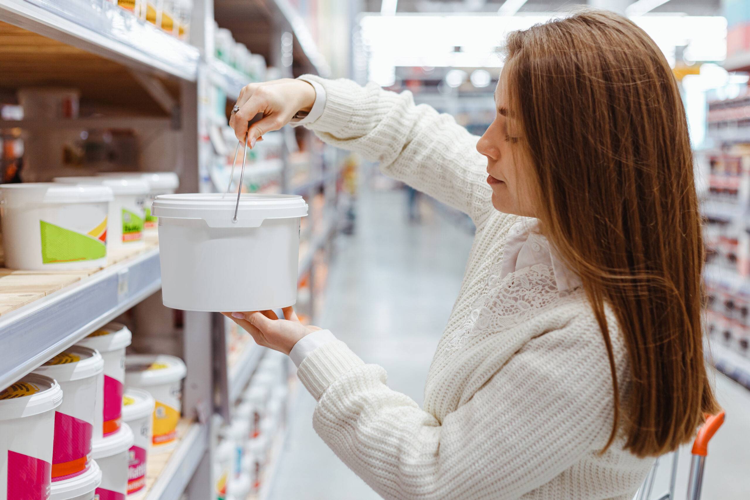 Young woman is choosing paint in buckets for walls in a hardware DIY Store. Acrylic paint for concrete surfaces in plastic buckets.