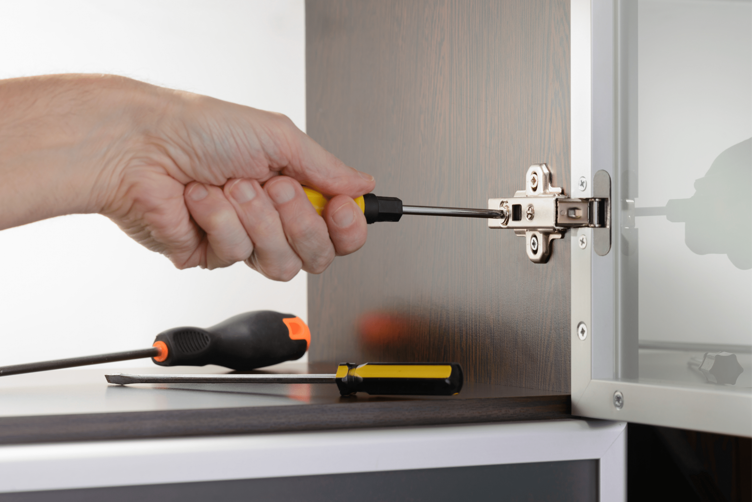 Closeup of a hand-using screwdriver to tighten cabinet hinge.