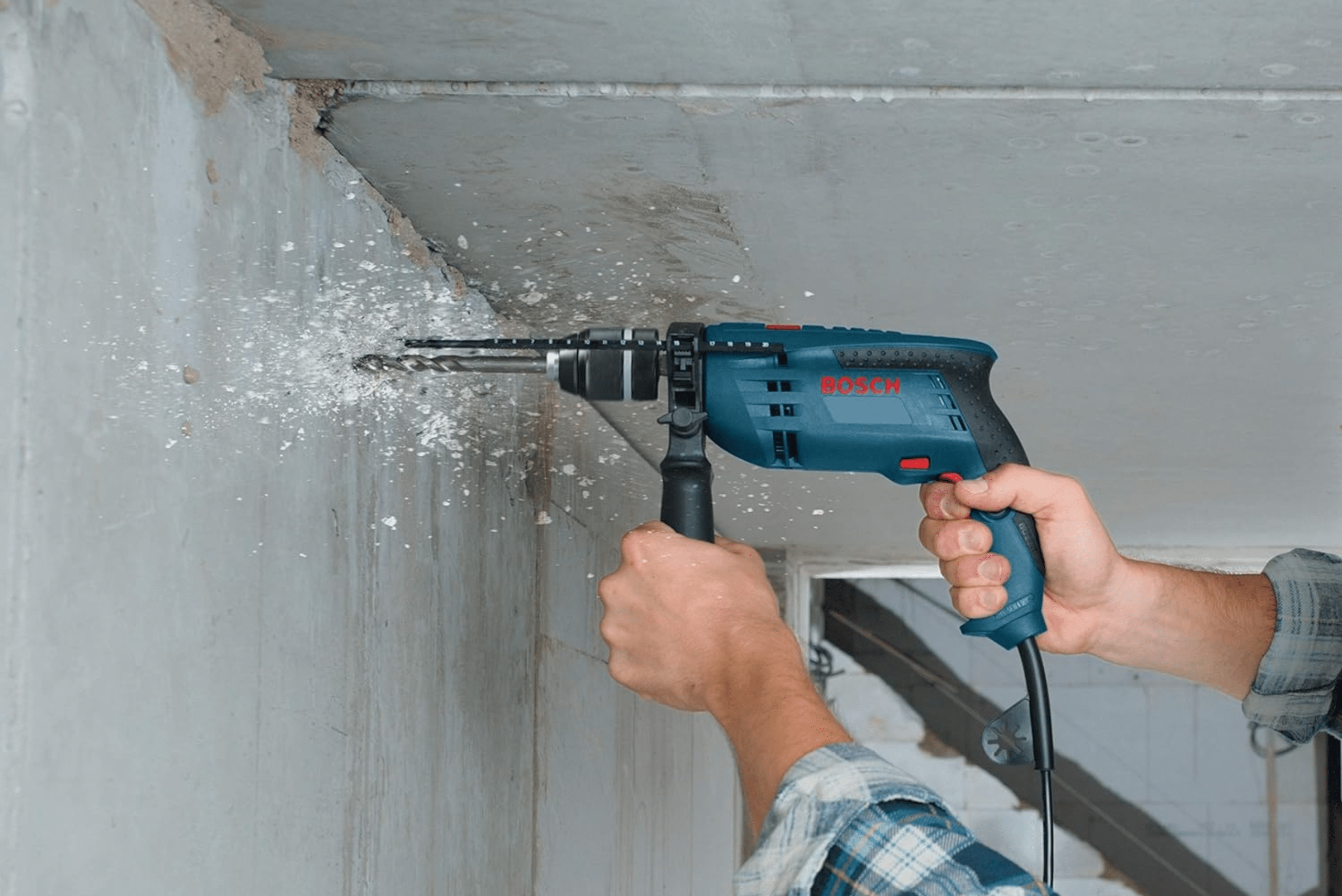 Person using hammer drill on concrete wall.