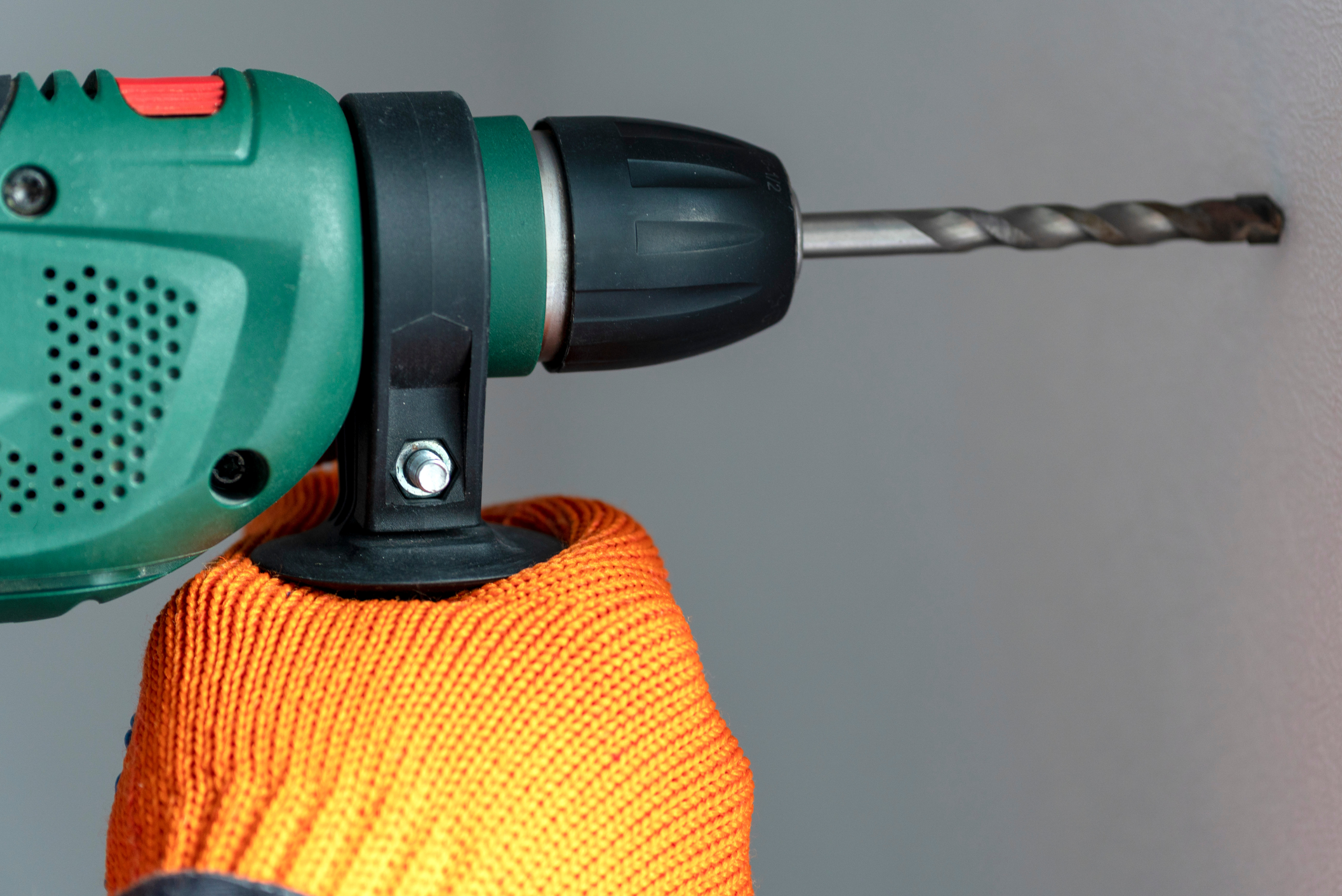 Closeup of hands wearing gloves using a hammer drill.