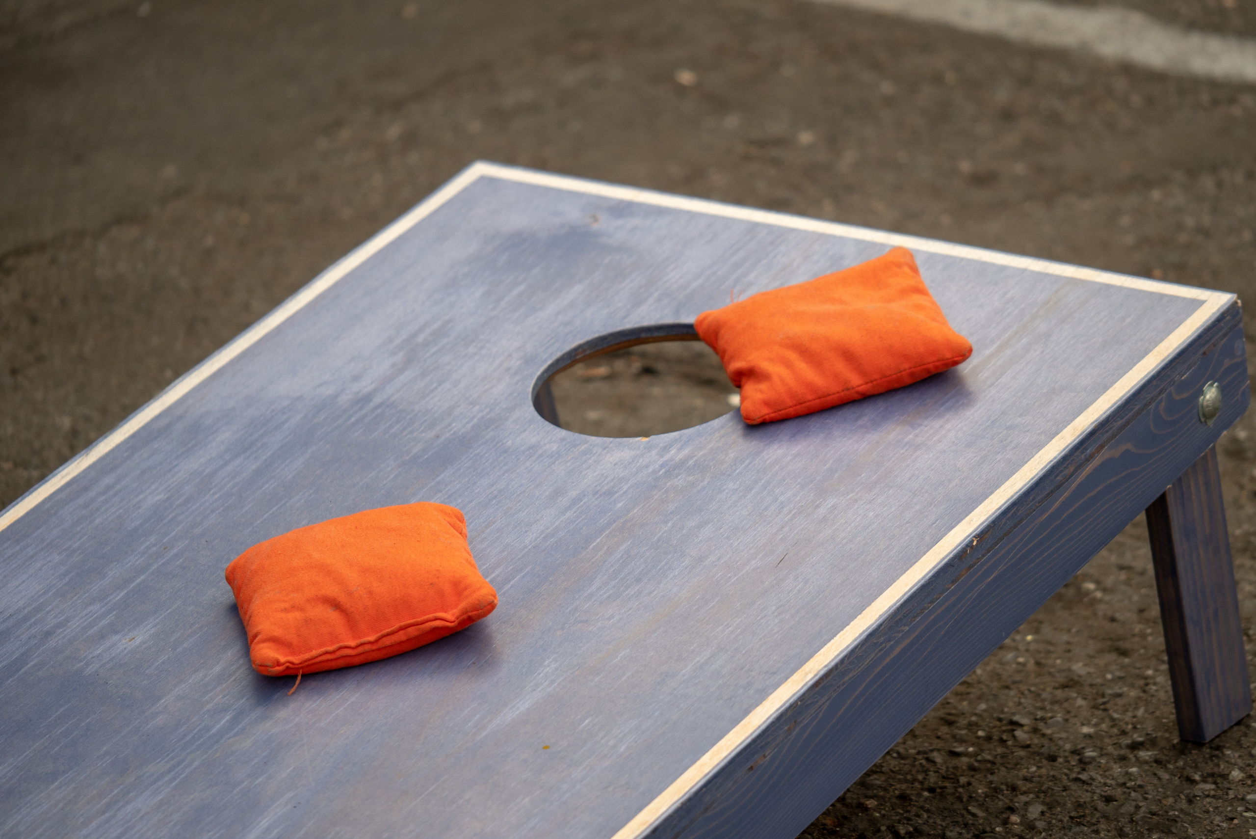 Cornhole board with two orange bags on top.