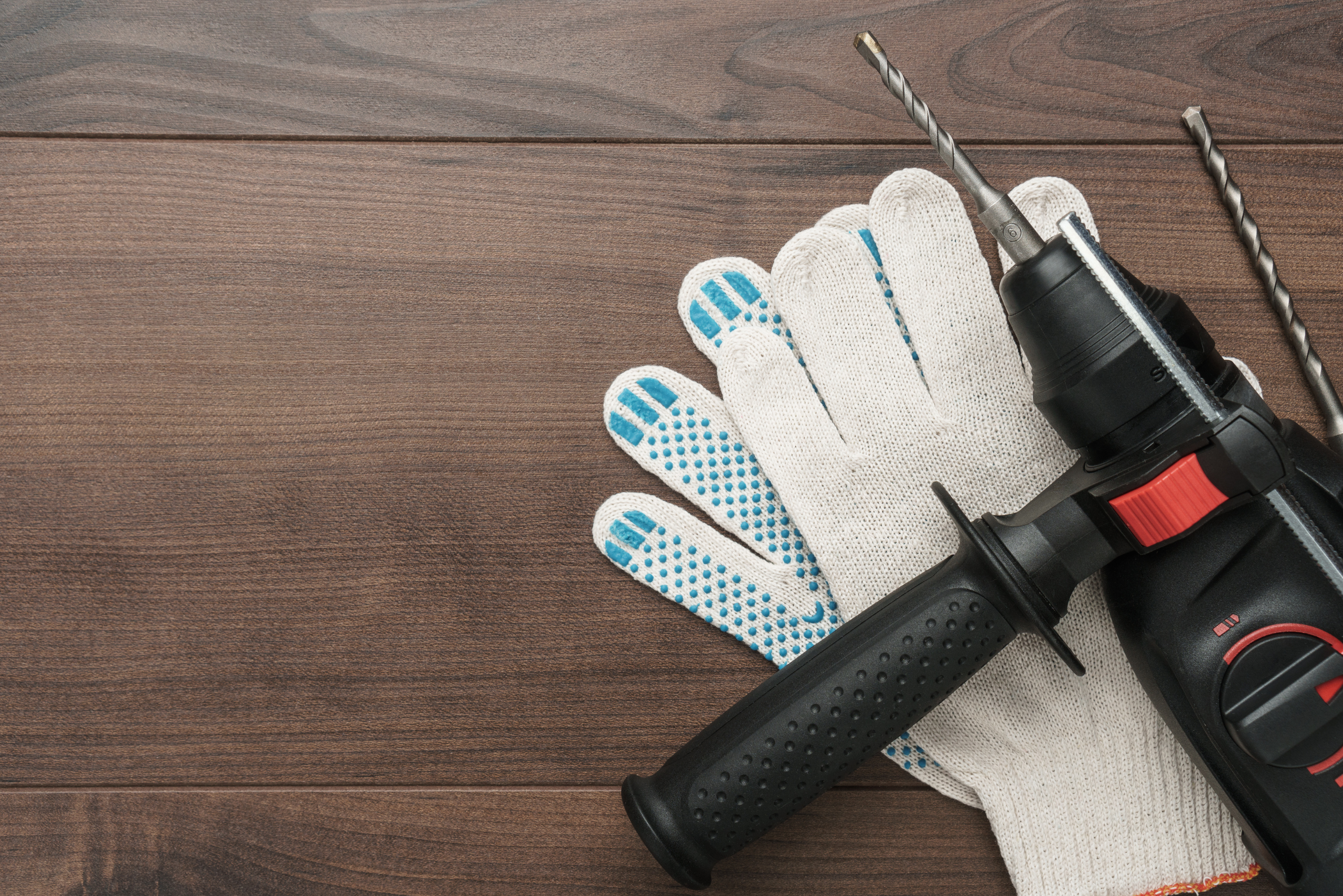Hammer drill on top of gloves on wood.