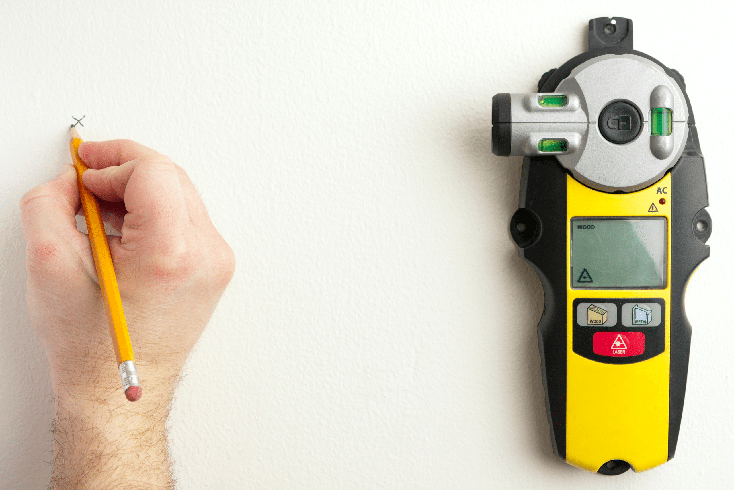 Hand using a pencil to mark the wall where indicated by a stud finder.