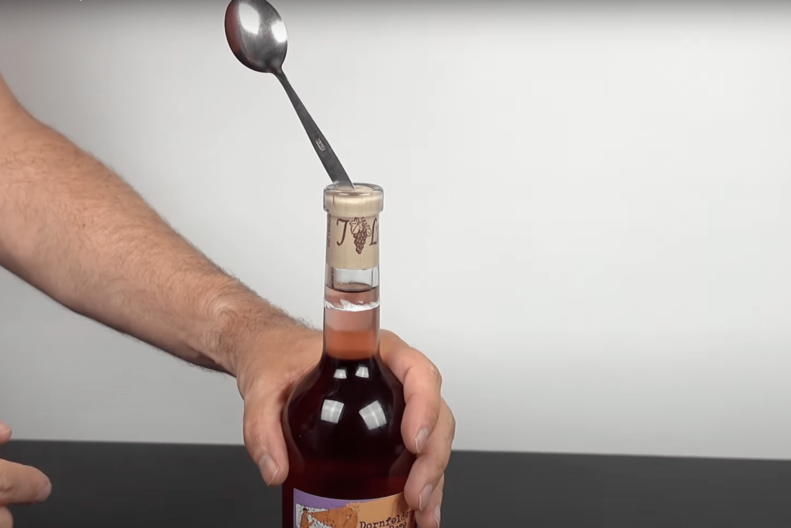 Person using spoon to open wine bottle.