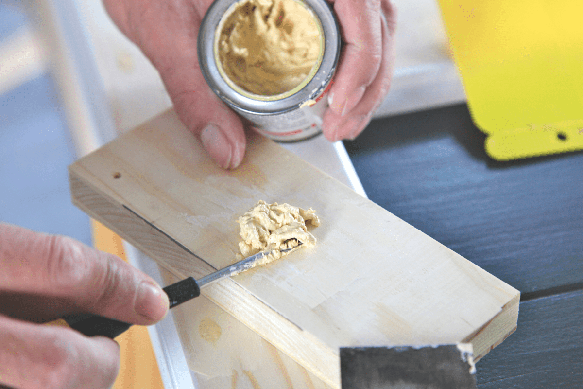 Preparation woodwork. Close-up putty cans in man's hand. DIY worker applying filler to the wood. Removing holes from a wood surface. Application of putty