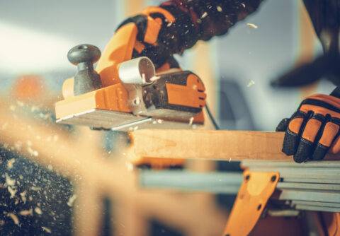 Caucasian Carpenter with Corded Wood Planer in His Hand Planing Wood Plank. Construction Site Theme.