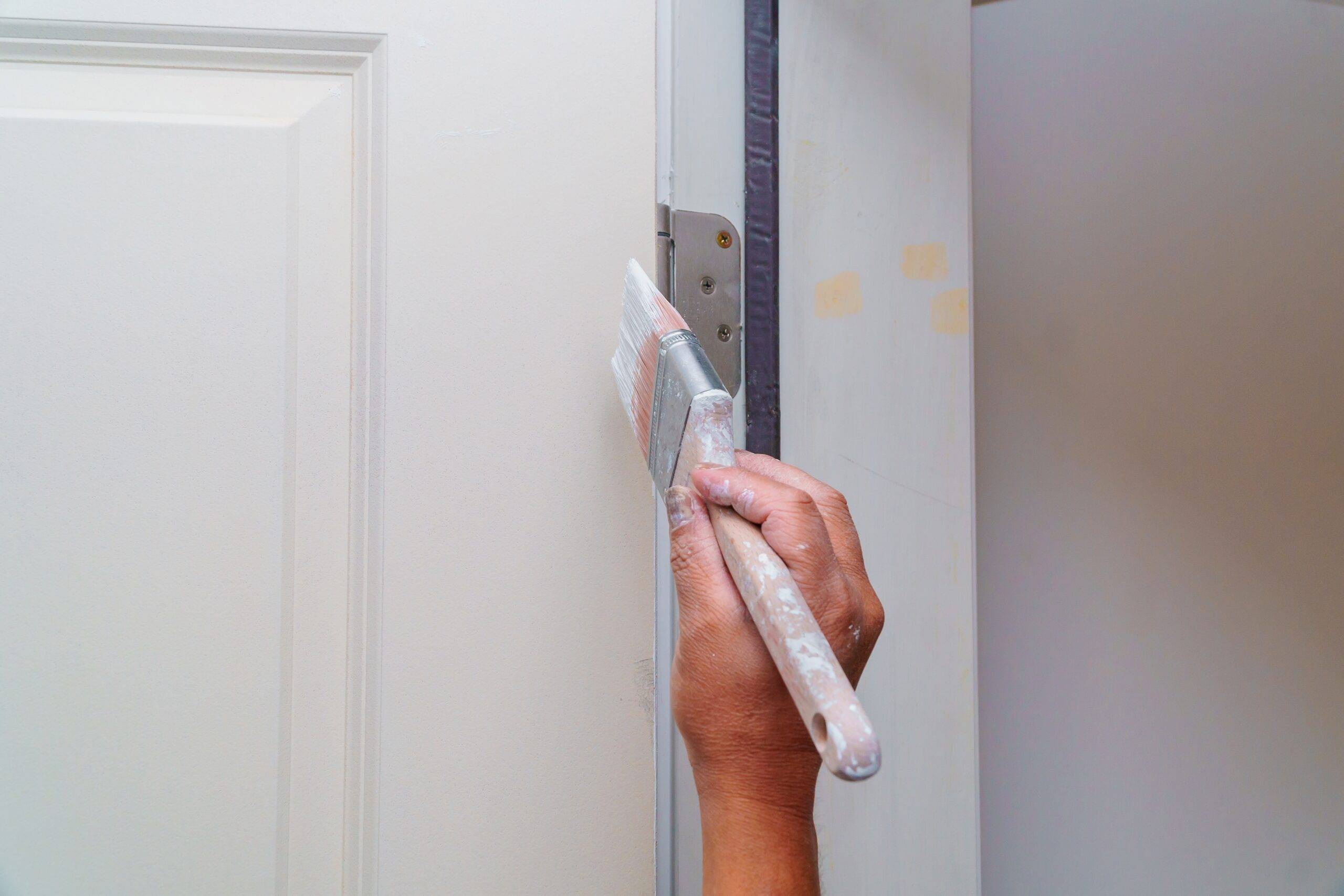 Contractor painting a wooden door white in a new house.