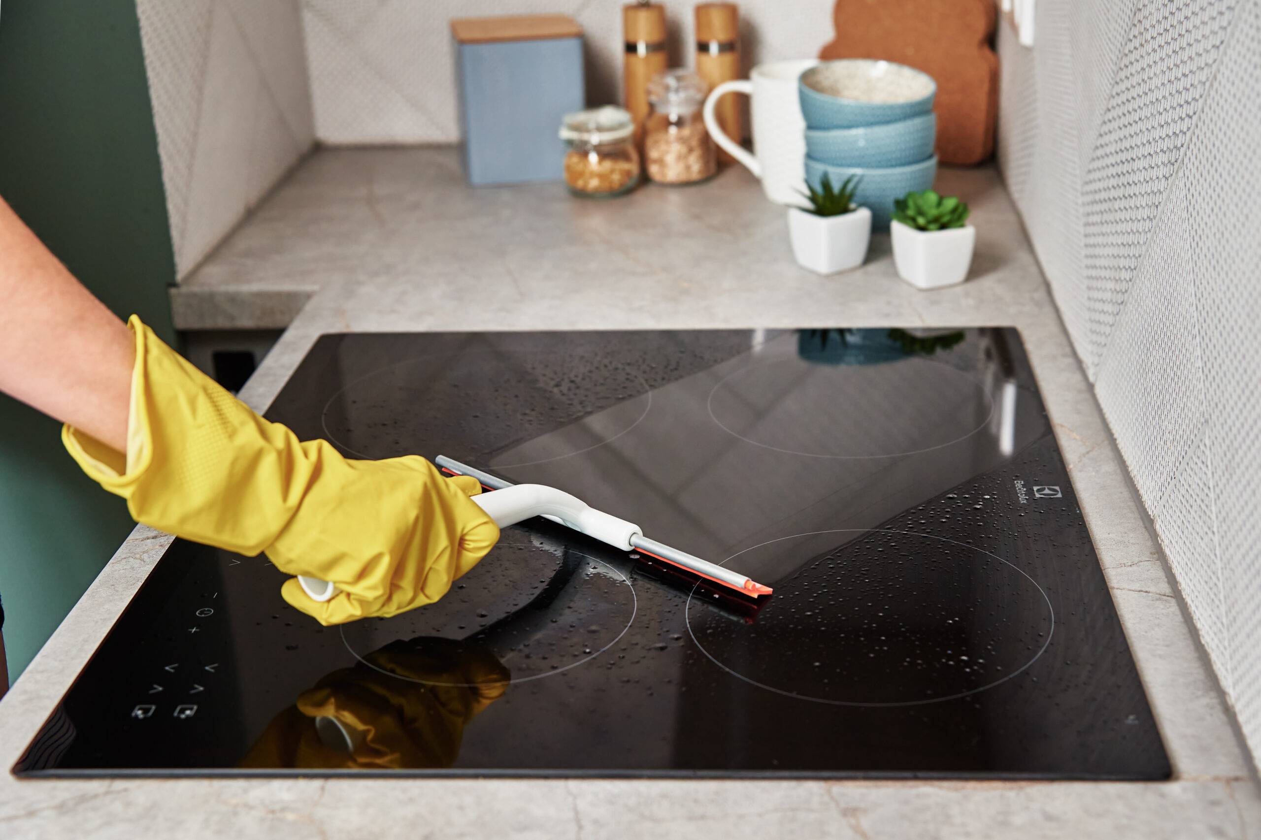 Cleaning induction stove. Woman in yellow rubber gloves cleans kitchen induction hob with cleaning spray.