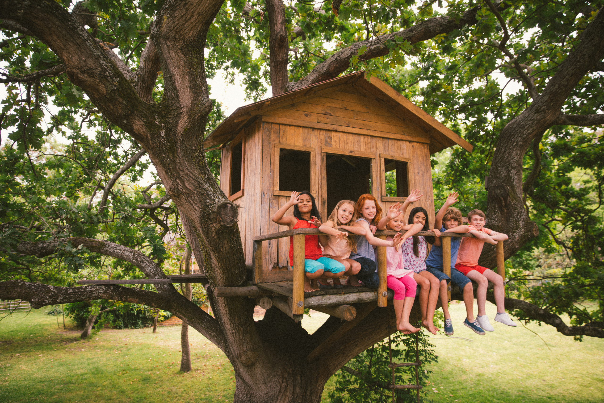 Bunch of kids sitting on the front of a treehouse.
