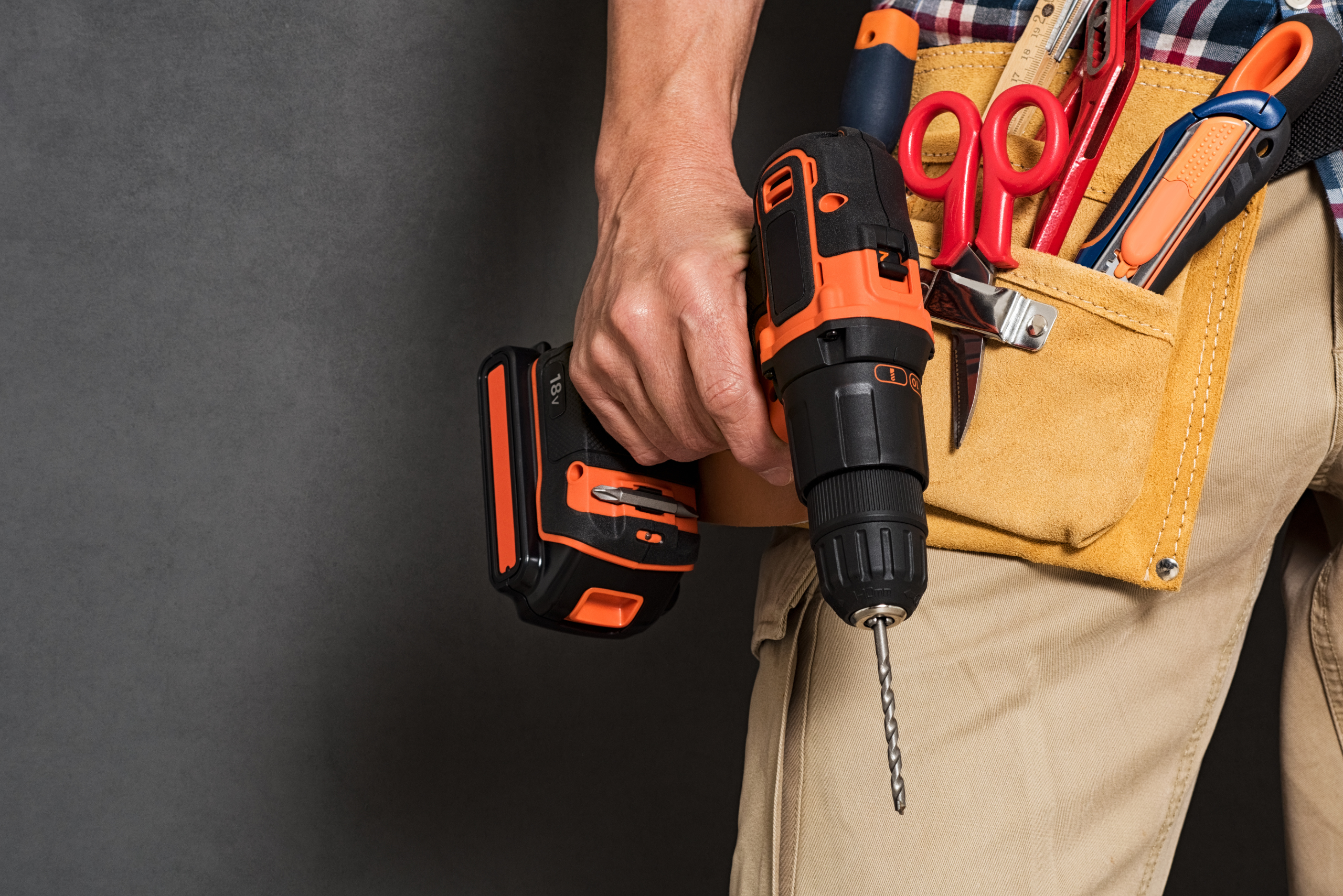 Man holding a drill in hand and wearing a tool belt.